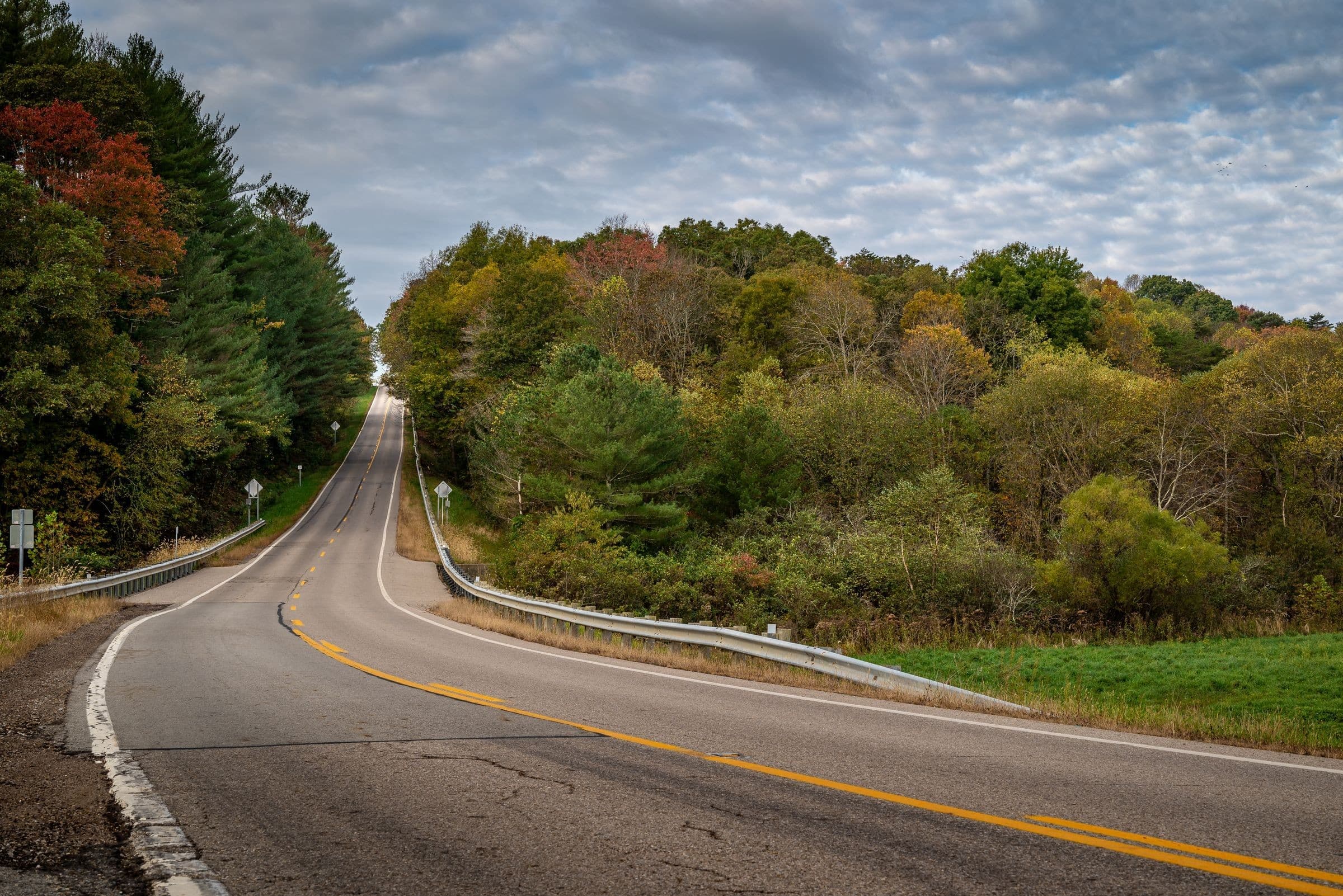 Towing Bartonville IL: curving two-lane road through wooded hills in autumn, the kind of road our trucks cover around Bartonville